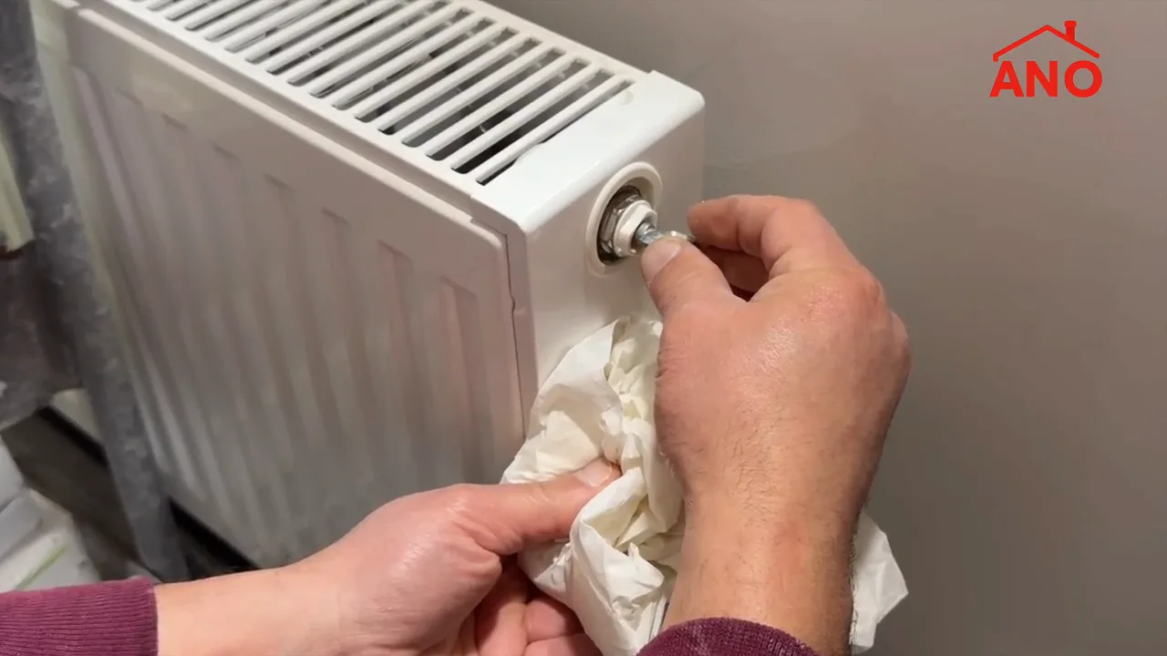 Handen met ontluchtingssleutel en opvangpapier bij een radiator