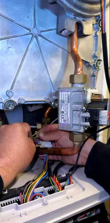 Handen bij een elektrische verbinding in de geopende ketel