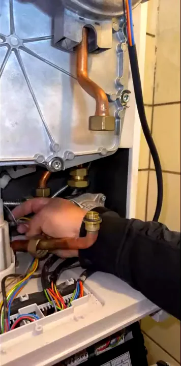 Hand onderzoekt bedrading onder in een geopende Intergas-ketel