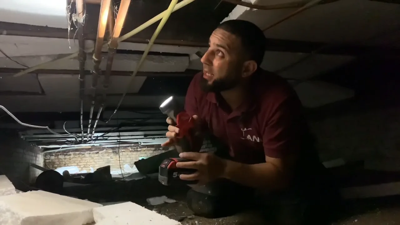 Anouar onderzoekt de leidingen onder de vloer met een lamp