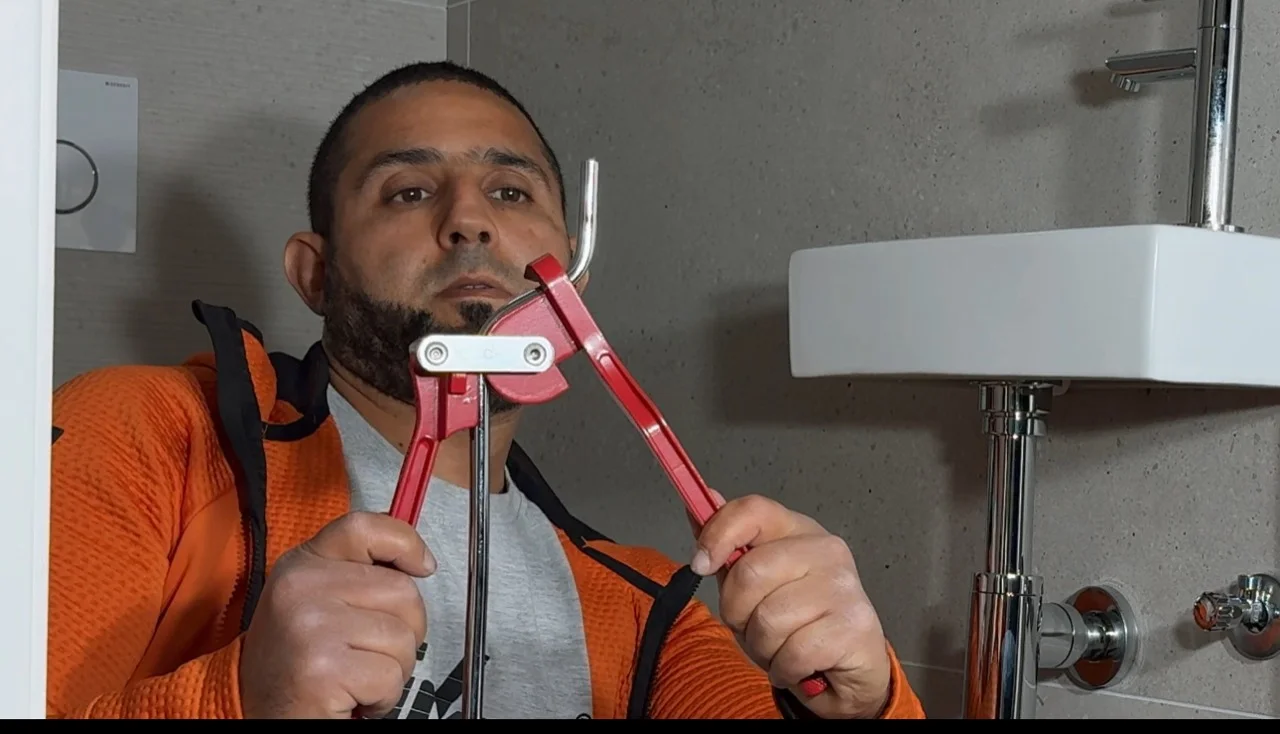 Anouar toont zichtbaar afvoerwerk onder een wastafel